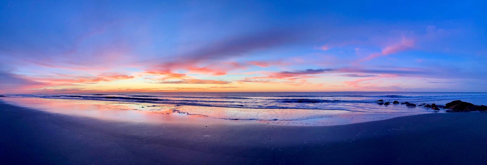 Dawn breaks in a swath of purple, orange, and blue over a sandy beach